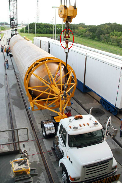 A rocket fuel tank lies lengthwise on truck one end is connected to a crane hook
